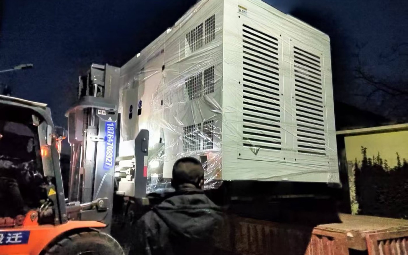 Wrapped silent generator enclosure being moved by forklift at night