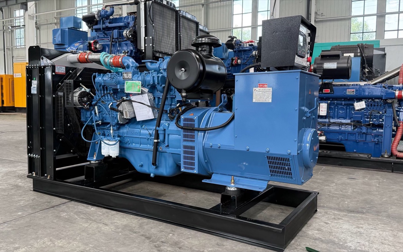 Blue open industrial generator sets on steel skids inside a workshop